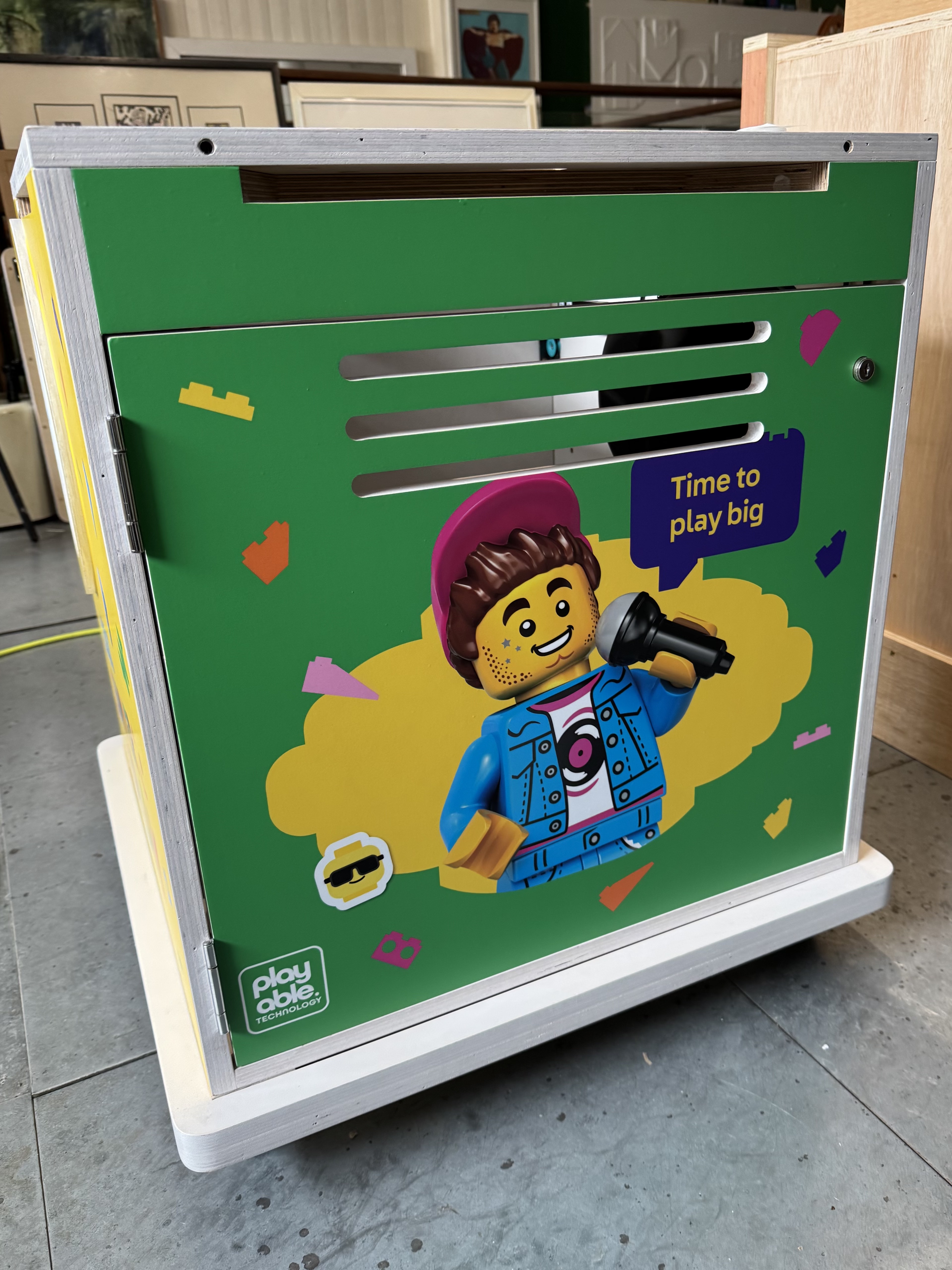 A BeatBricks unit in the Playable workshop, its green side panel showing LEGO Summer of Play graphics and a minifigure singing into a microphone, captioned 'Time to play big'.