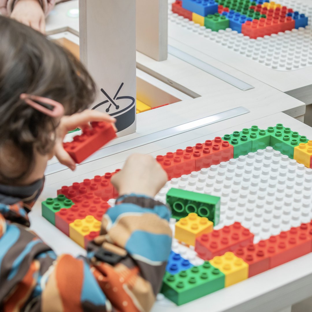 A child places DUPLO bricks onto the BeatBlocks Live baseplate.