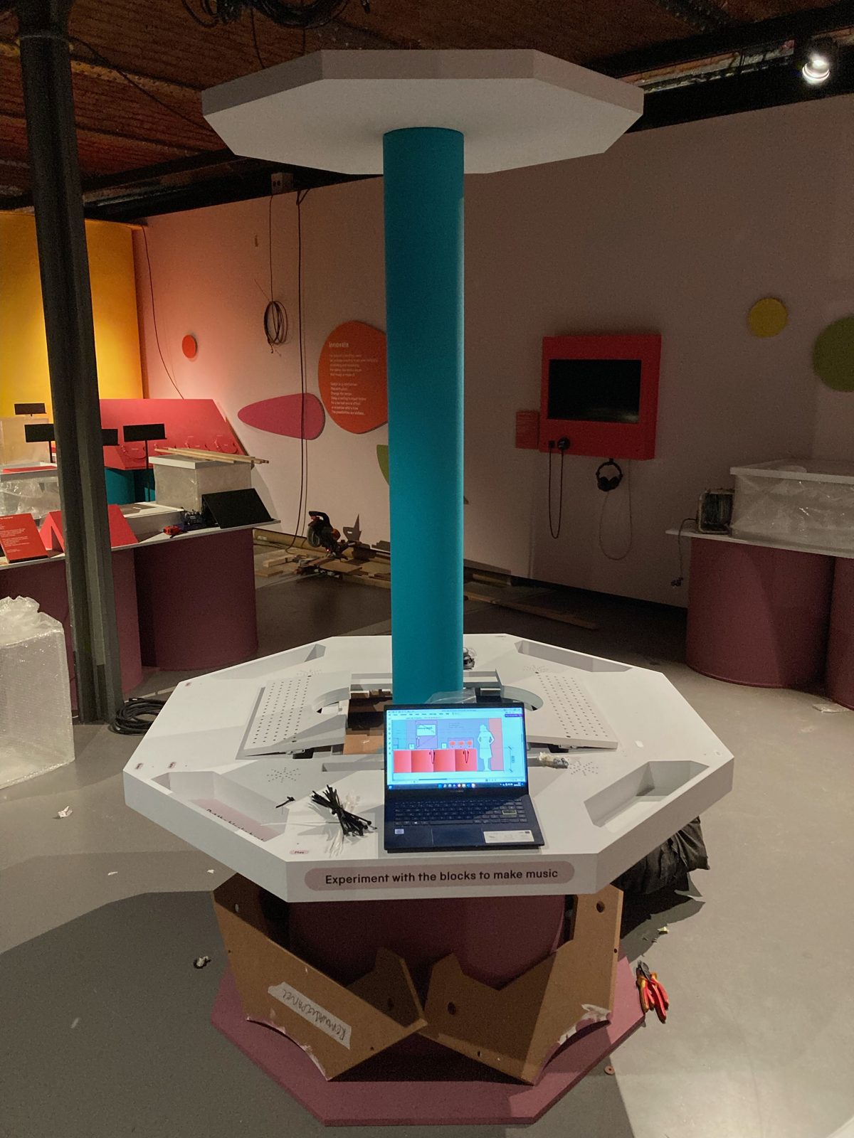 The Music Maker exhibit during install, a laptop showing a design elevation of the exhibit on the part-built table, with the gallery still under construction around it.