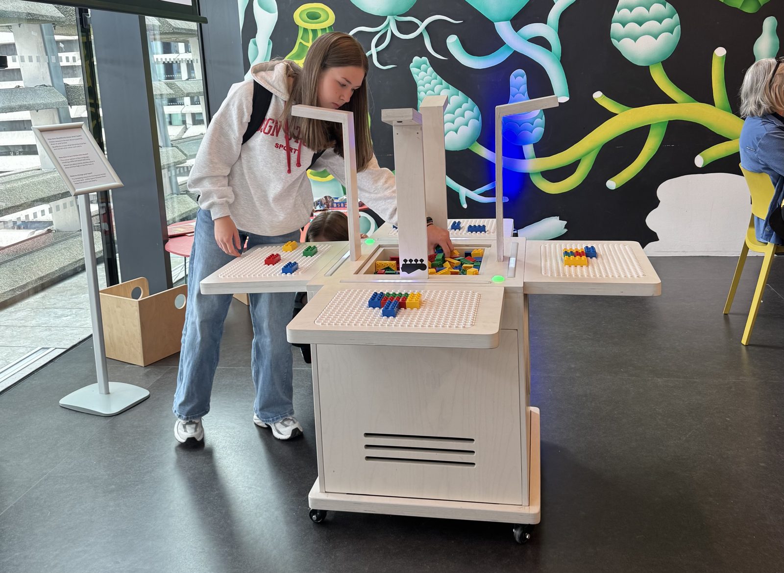A visitor plays the full BeatBlocks Live unit in V&A Dundee's Robertson Studio, a colourful mural behind and the Dundee skyline through the window.