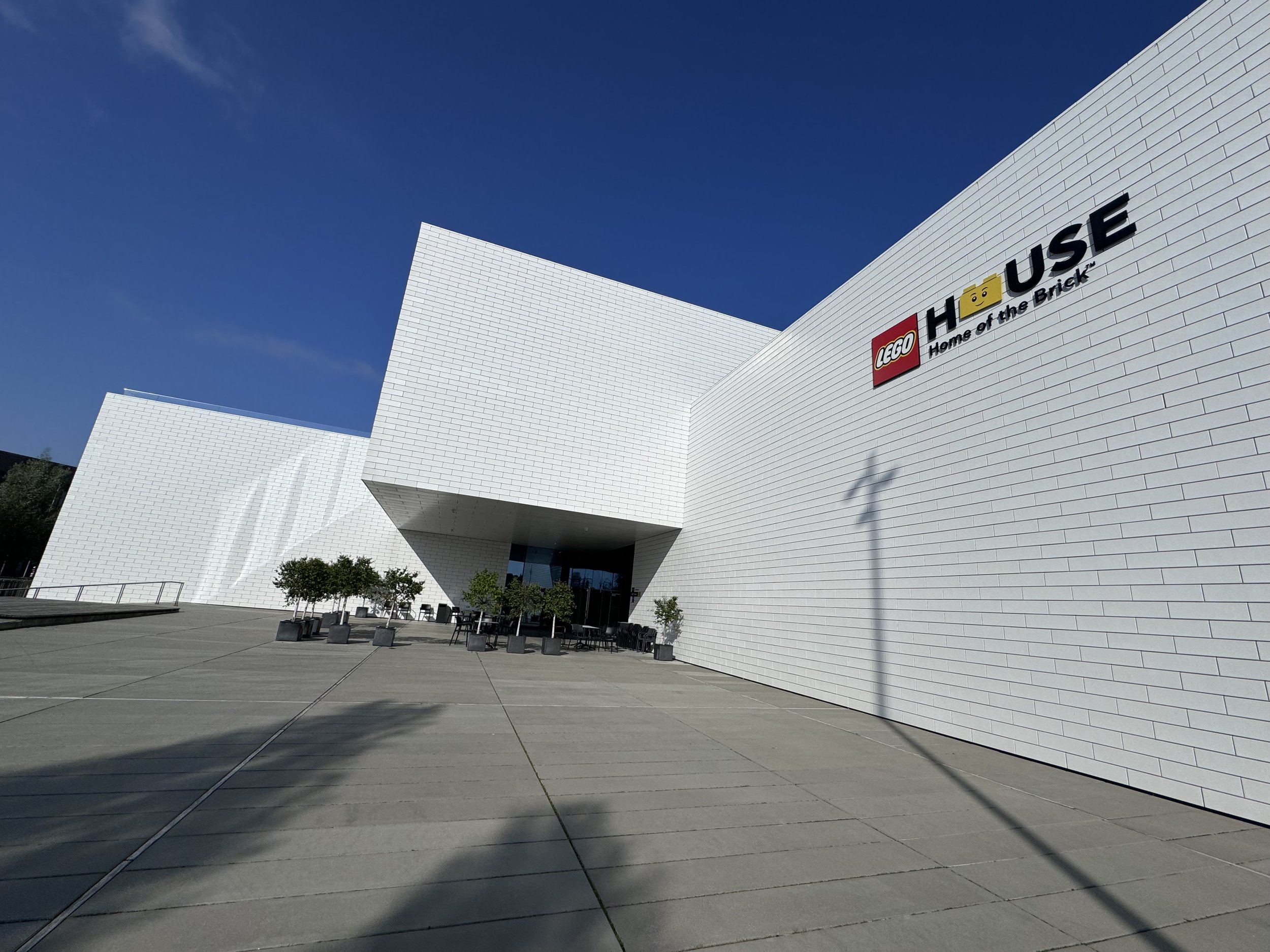 A view from outside the main entrance to the LEGO House in Billund, a striking angular white building against a blue sky.