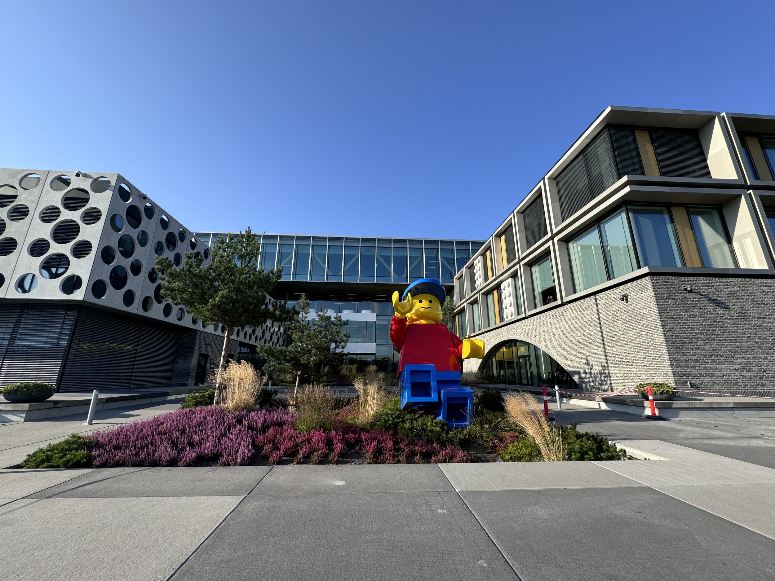 LEGO headquarters in Billund on a sunny day; outside the main entrance stands a giant LEGO minifigure in a red top, blue trousers and a baseball cap.