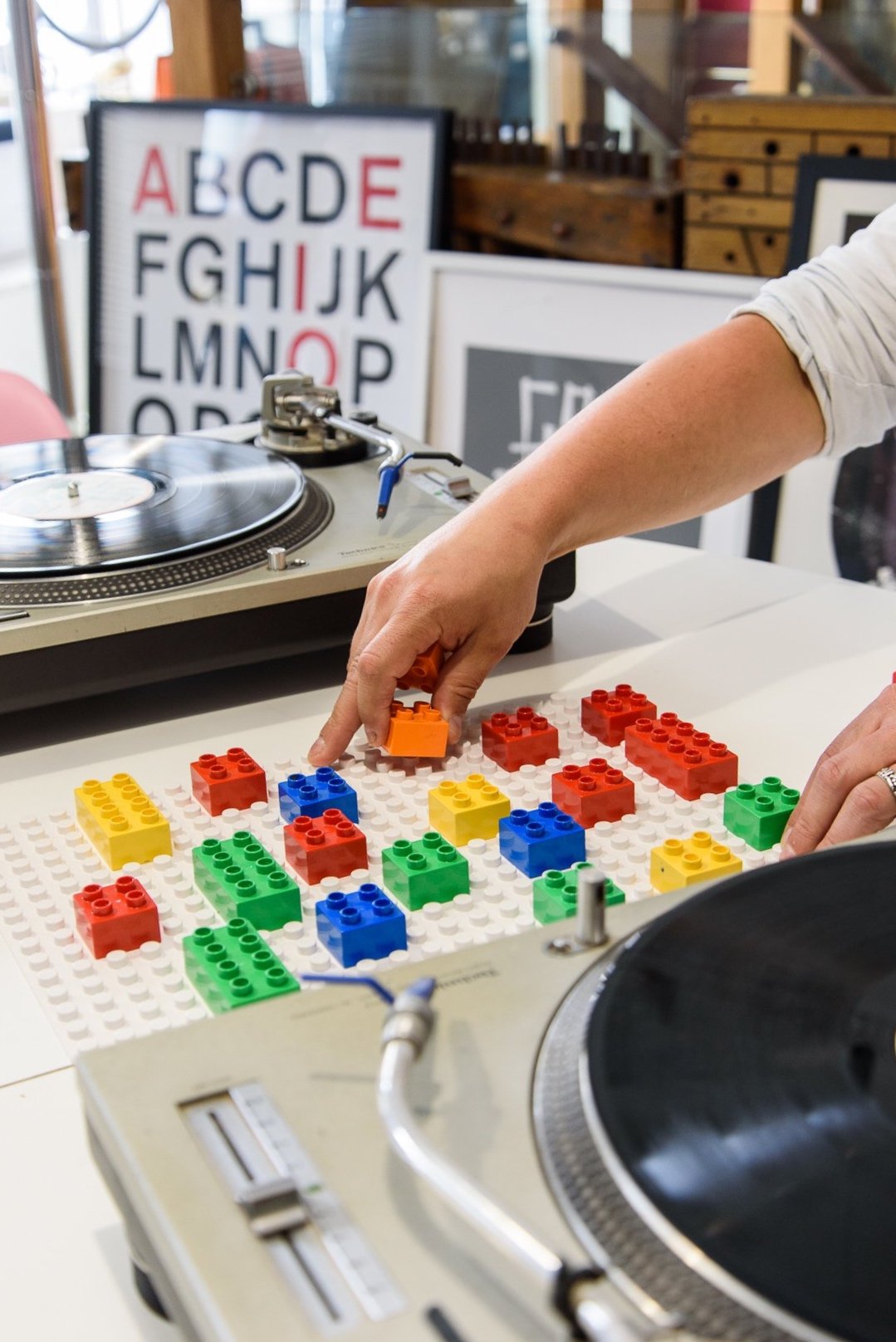 Hands place DUPLO bricks on a baseplate set between two DJ decks.